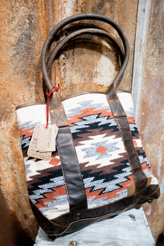 Handbag with patterned design and leather accents against a textured background