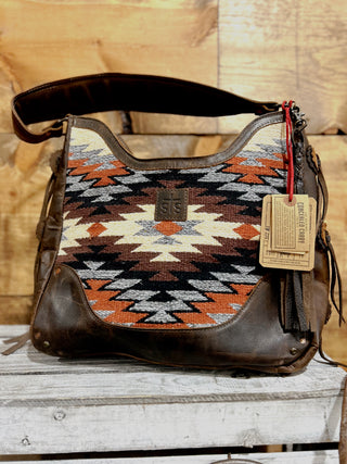 Brown leather handbag with a patterned flap on a wooden surface