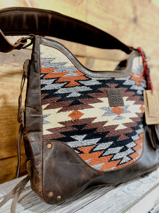 Brown leather bag with patterned fabric interior on a wooden surface