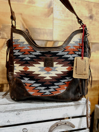 Handbag with geometric pattern and leather accents on a wooden surface