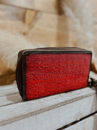 Red textured wallet on a wooden surface with a blurred natural background