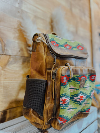 Brown leather backpack with colorful patterned flap on a wooden surface