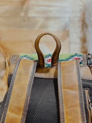 Close-up of a backpack with leather straps and colorful patterned fabric.
