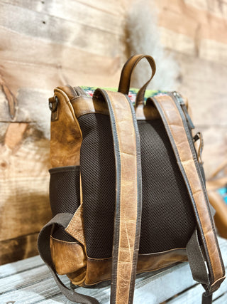 Brown leather backpack with black mesh padding on a wooden surface