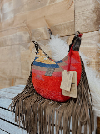 Red woven handbag with fringes and a tag on a wooden surface