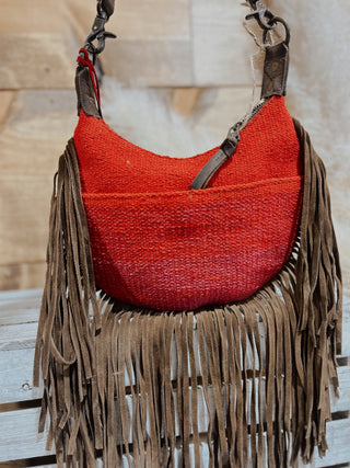 Red woven handbag with brown fringe on a wooden surface