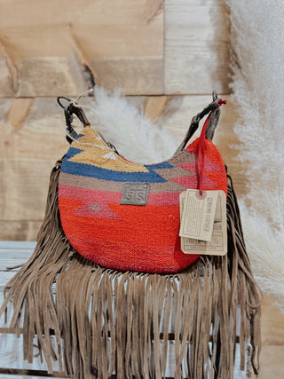 Colorful woven handbag with fringe on a wooden surface