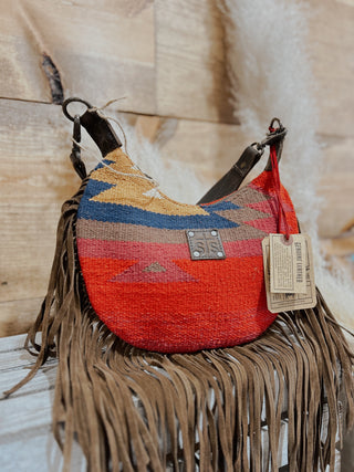 Colorful woven handbag with fringe and a tag on a wooden surface