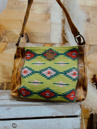 Handbag with a green patterned front section on a wooden surface