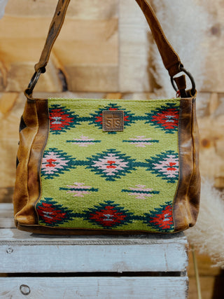 Handbag with green patterned top and brown leather sides on a wooden surface
