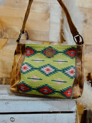 Handbag with green patterned fabric and brown leather accents on a wooden surface.
