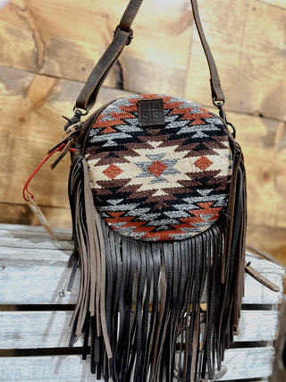 Round handbag with tribal pattern and fringes on a wooden surface