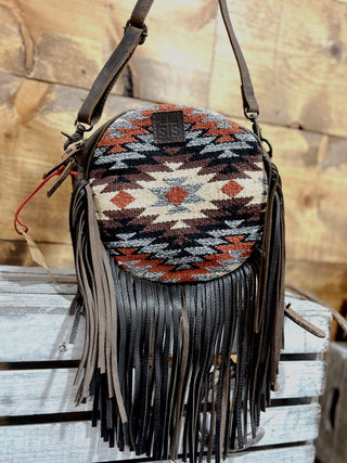 Round handbag with tribal pattern and fringes on a wooden surface