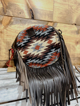 Round handbag with tribal pattern and fringes on a wooden surface