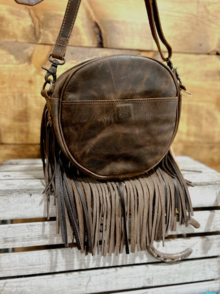 Brown leather handbag with fringe on a wooden surface