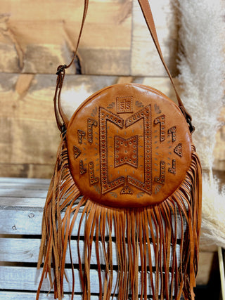 Brown leather handbag with fringe on a wooden surface