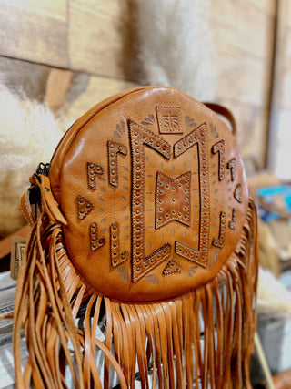 Brown leather bag with intricate designs and fringes on a wooden surface
