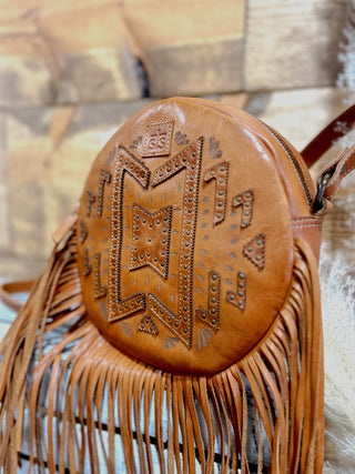Brown leather handbag with fringe details and embossed design on a blurred background