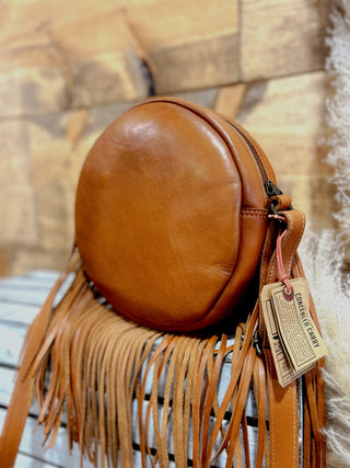 Brown leather handbag with fringe details and a tag on a textured surface