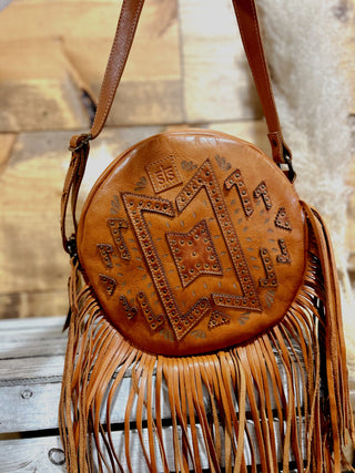 Brown leather handbag with fringe details on a wooden surface