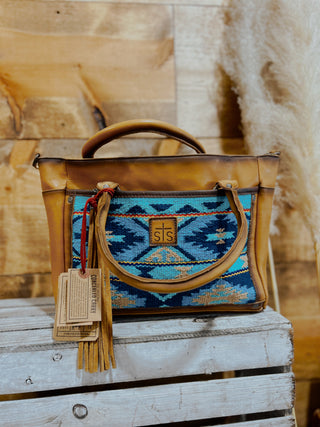 Leather handbag with blue pattern and visible brand tag on a wooden surface