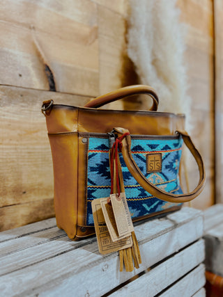 Brown leather handbag with blue patterned strap on a wooden surface