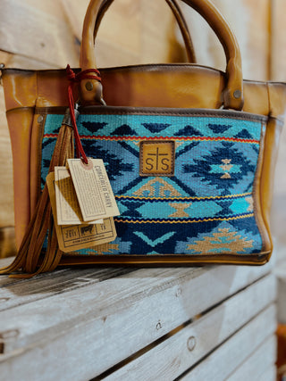 Brown leather handbag with blue geometric pattern on a wooden surface