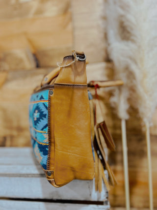Brown leather bag with colorful pattern on a wooden surface