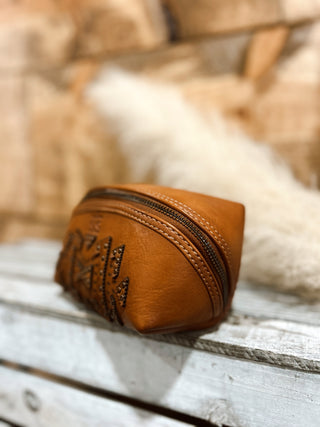 Brown leather pouch with a zipper on a wooden surface with a blurred natural background