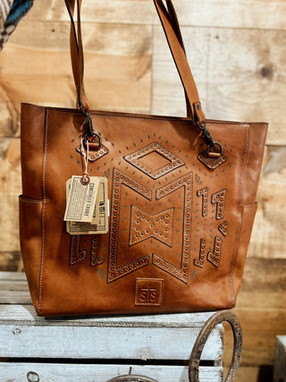 Brown leather tote bag with embossed design on a wooden surface