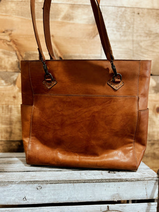 Brown leather tote bag on a wooden surface with a rustic background