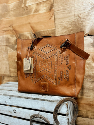 Brown leather handbag with embossed designs on a wooden surface
