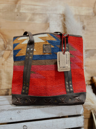 Handbag with geometric pattern and leather straps on a wooden surface