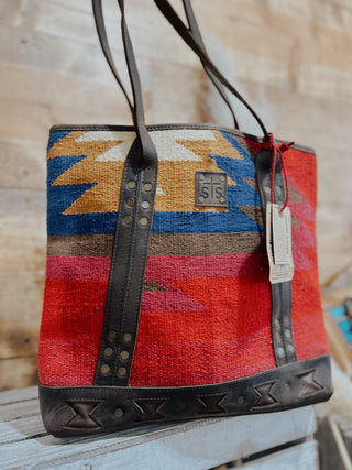 Handbag with colorful pattern and leather straps on a wooden surface