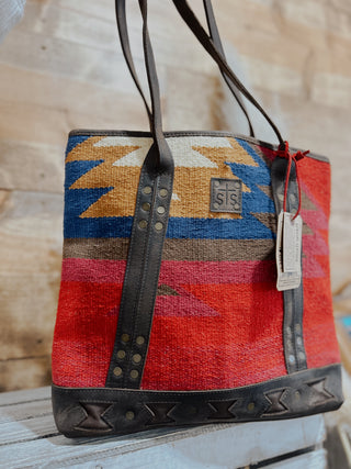 Handbag with colorful pattern and leather straps on a wooden surface