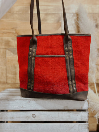 Red tote bag with brown handles and trim on a wooden surface