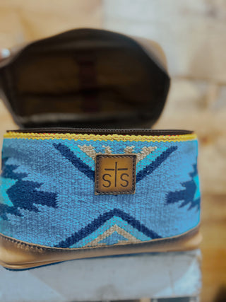 Blue patterned pouch with a gold zipper and 'sts' logo on a blurred background