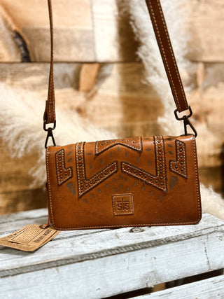 Brown leather handbag with intricate designs on a wooden surface