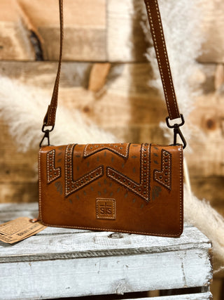 Brown leather handbag with intricate designs on a wooden surface