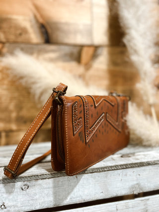 Brown leather clutch with intricate designs on a wooden surface
