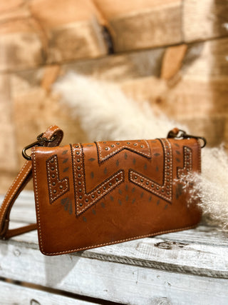 Brown leather handbag with intricate designs on a wooden surface