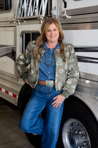 Woman in a camouflage jacket and blue jeans standing in front of a large truck.