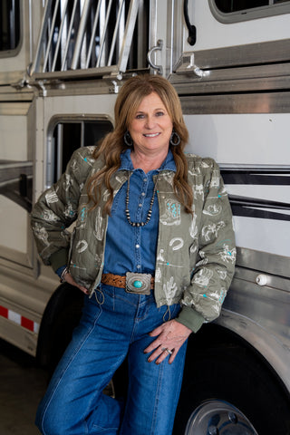 Woman standing in front of a large truck wearing a patterned jacket and blue jeans.