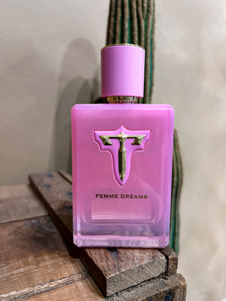 Pink perfume bottle labeled 'Femme Dreams' on a wooden surface with a cactus in the background.