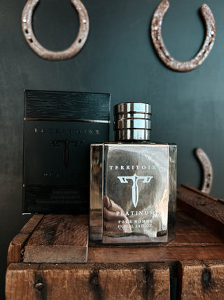 Território perfume bottle and packaging on a wooden surface with horseshoes in the background.