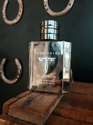 Silver perfume bottle labeled 'Territoire Platinum' on a wooden surface with horseshoes in the background.