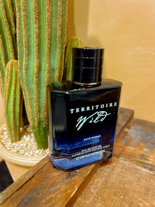 Black perfume bottle labeled 'Territoire' on a wooden surface with a cactus in the background.