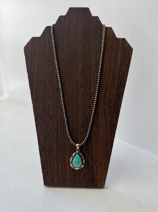 Necklace with a turquoise pendant on a wooden stand against a white background