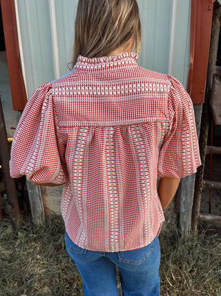Person wearing a red and white checkered blouse with puffed sleeves in an outdoor setting.