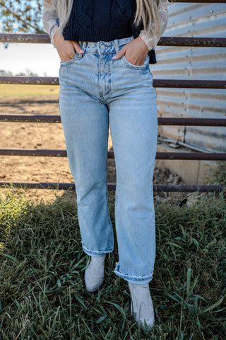 Person wearing light blue jeans standing in a grassy field with a metal fence in the background.